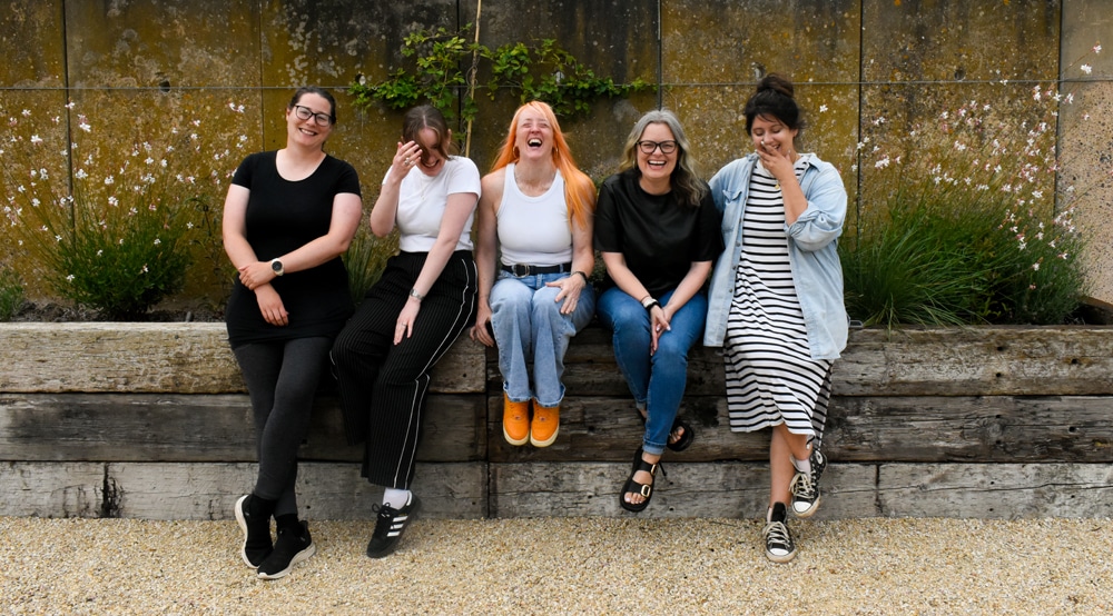 Photo of The Better Content Club ™️Team with Alice, Georgia, Nat, Polly and Victoria sitting on a bench laughing