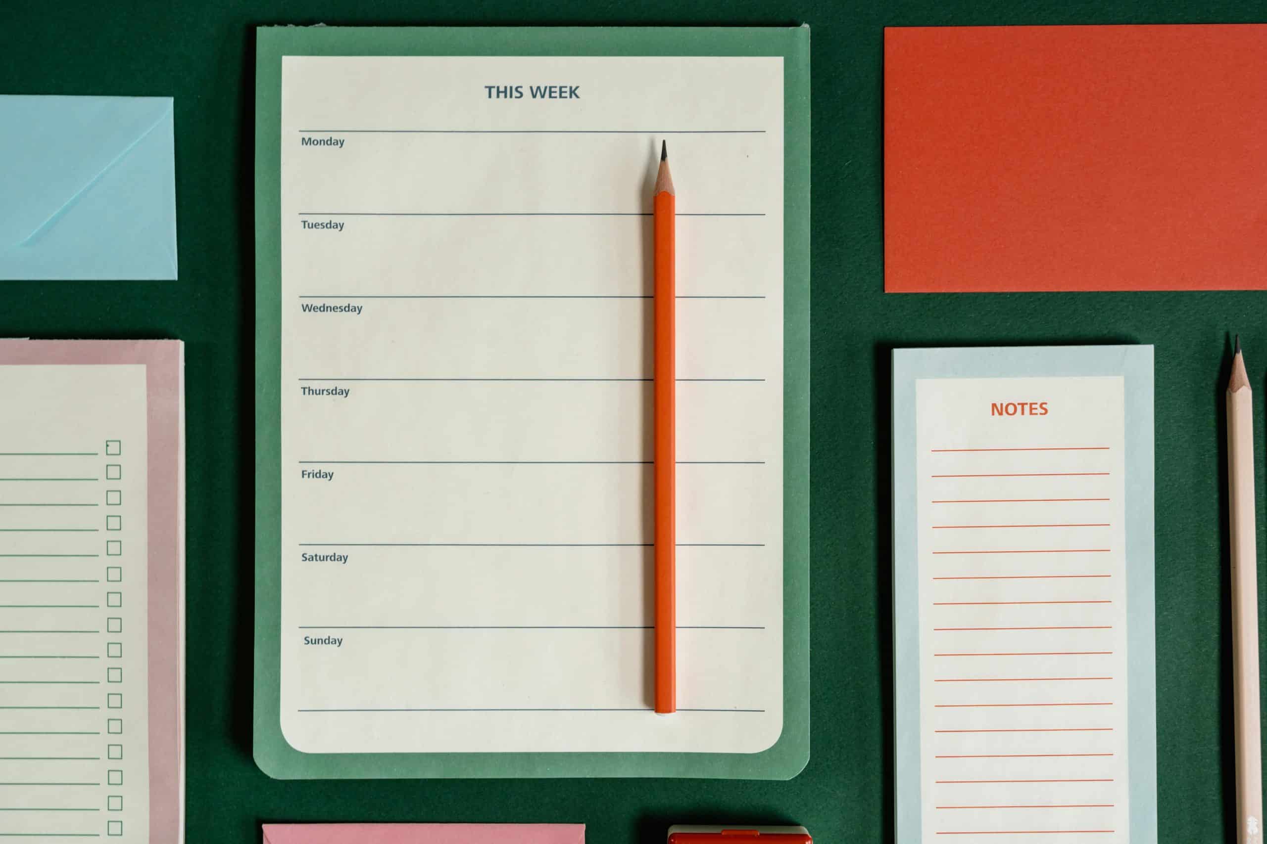 A number of note pads on a table one with "this week" and the days of the week on it, another "notes" with lines an another with checkboxes.